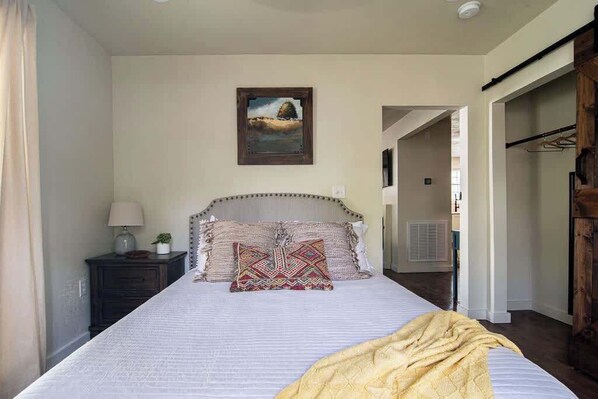 Un dormitorio con una cama grande, una mesita de noche, una lámpara, un cuadro en la pared y una puerta de madera.