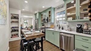 Une cuisine moderne avec des meubles de couleur verte, des appareils en acier inoxydable et une table à manger en bois.