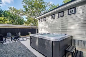 A hot tub in a backyard with a wooden deck, chairs, and a wooden fence.
