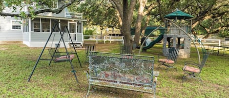 A playground with a swing set, a bench, and a tree.