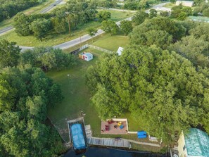An aerial view of a property with a swimming pool, a fenced area with outdoor seating, and a road in the background. - Red Bird Cabin - Studio Retreat (Kingsland)