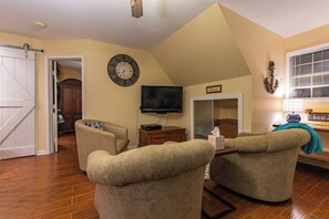 A living room with two armchairs, a flat-screen TV, a clock, and a sliding door leading to another room. - Red Bird Cabin - Studio Retreat (Kingsland)