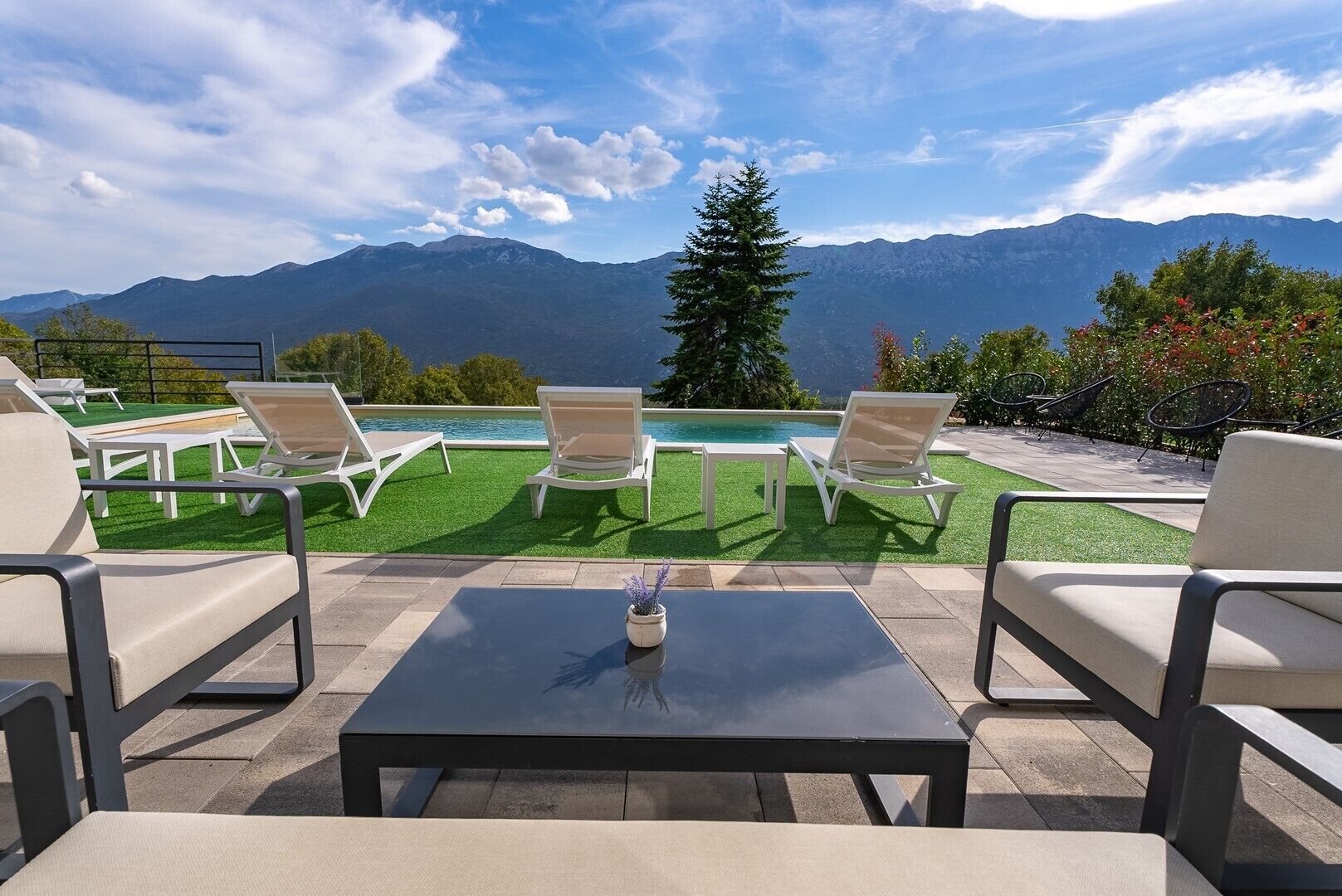Ein Poolbereich mit Liegestühlen und einem Tisch mit Blick auf ein Gebirge.
