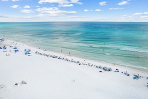 A beach with white sand and clear blue water. There are umbrellas and beach chairs along the shore.