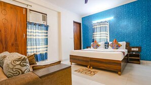 A bedroom with a bed, a wooden wardrobe, a small table, and a blue accent wall. - Fabexpress Mirage (New Delhi)