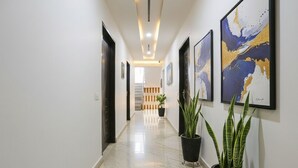 A hallway with a marble floor, potted plants, and framed artwork on the walls. - Fabexpress Mirage (New Delhi)