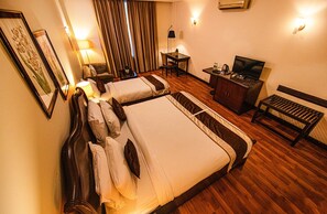 A hotel room with two beds, a desk with a chair, a TV, and a bench.