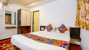 A hotel room with a large bed, a wardrobe, a mirror, and a ceiling fan. - FabHotel Sai Chatra (Nashik)