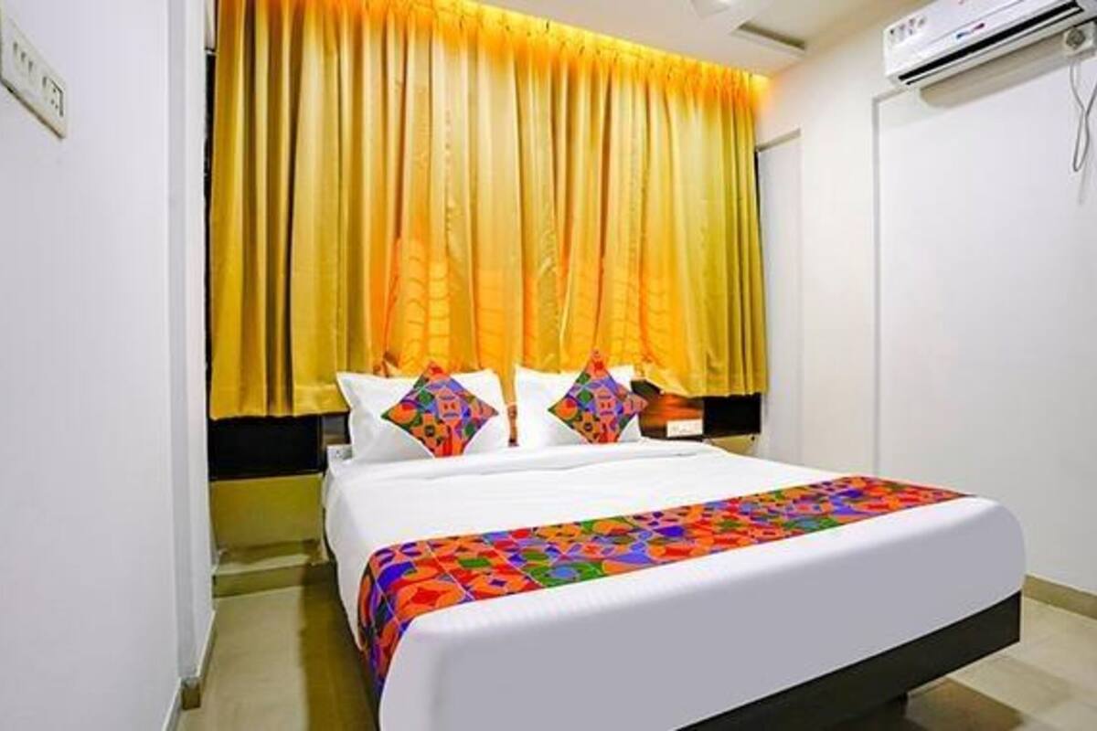 A bed with a colorful blanket, a yellow curtain, and a white wall.