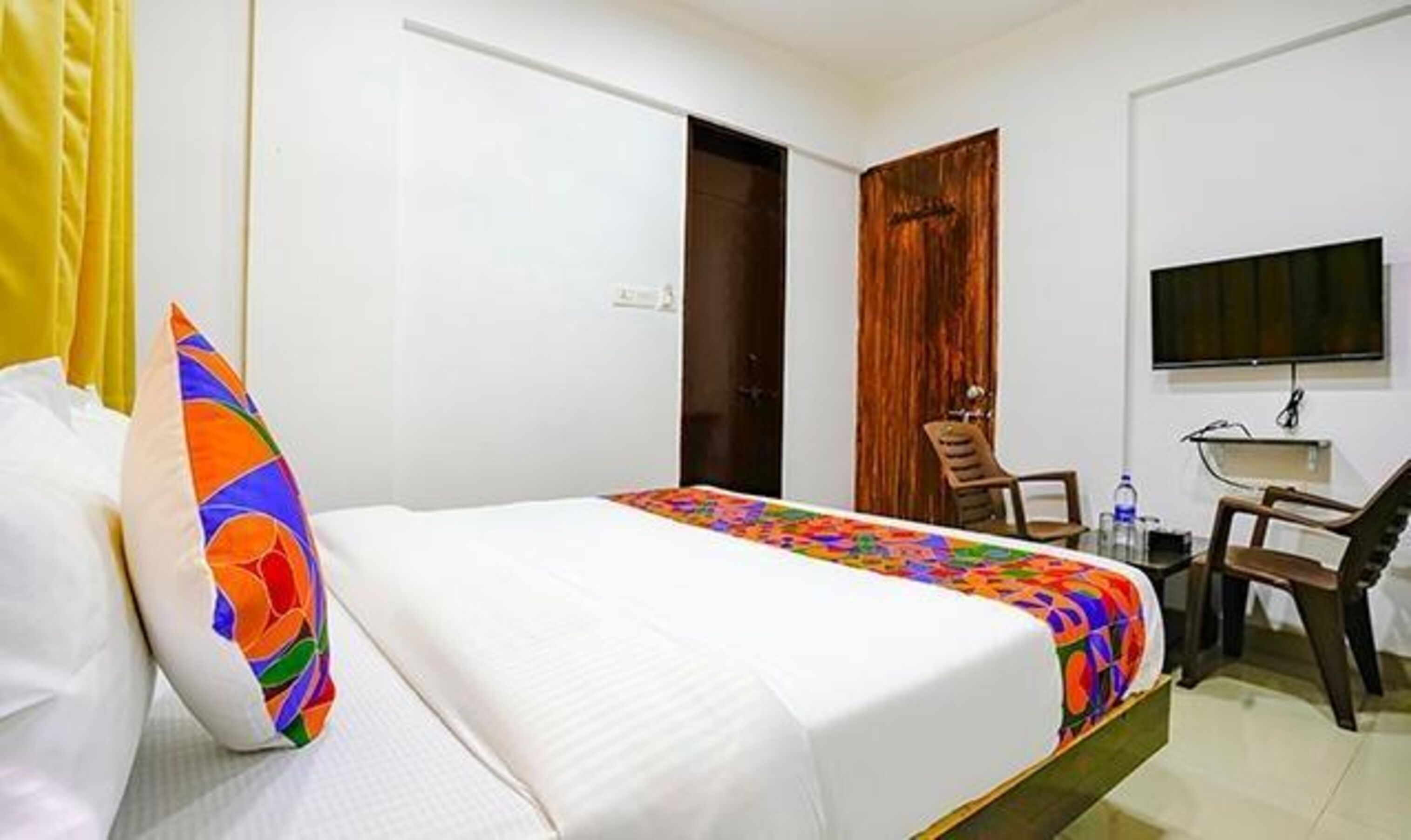 A hotel room with a bed, a desk, a chair, a television, and a door.