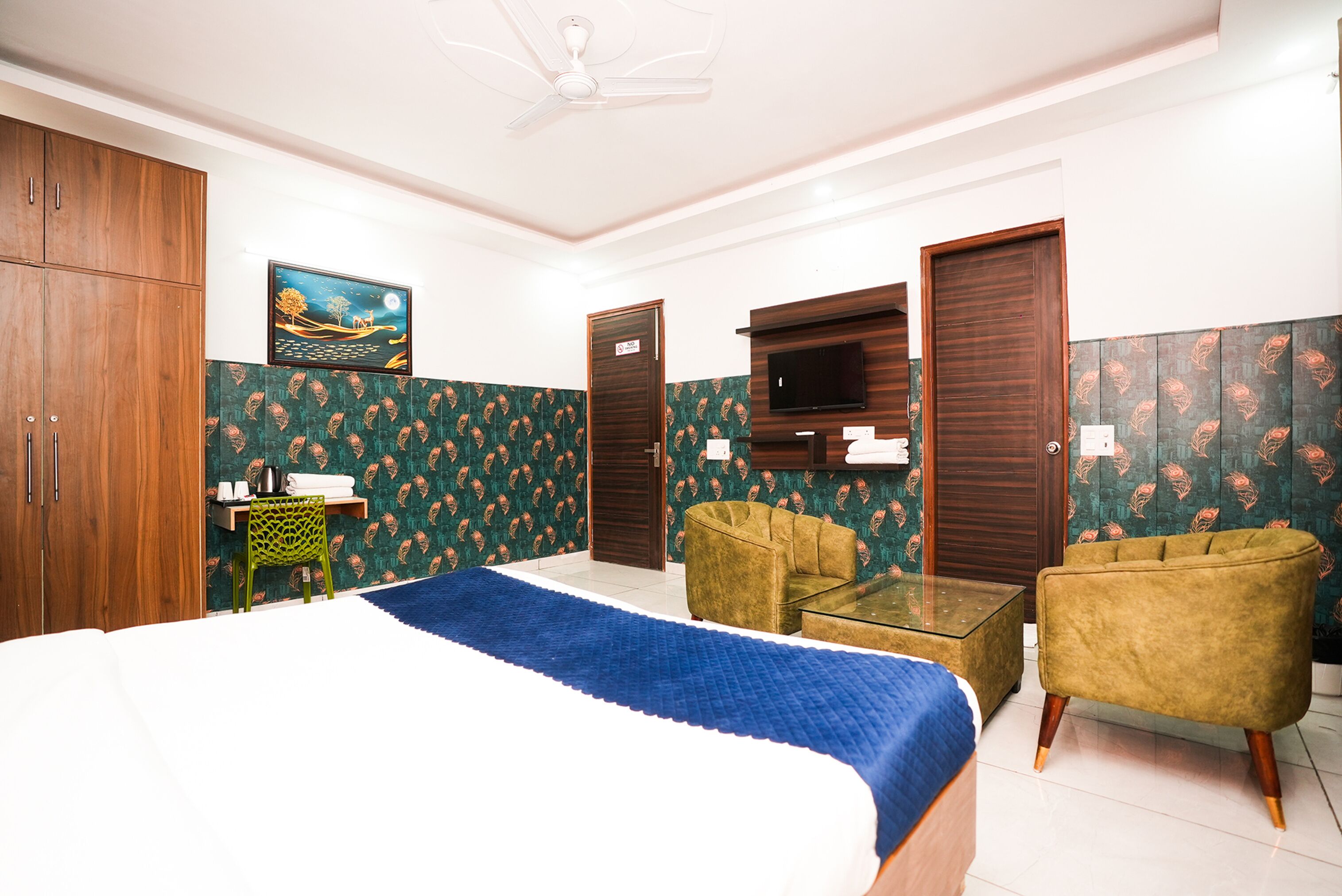 A hotel room with a bed, two armchairs, a small table, a TV, and a wardrobe.