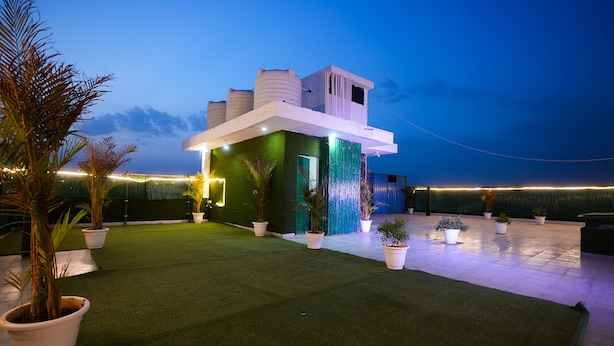 A modern building with a flat roof, surrounded by artificial grass and potted plants. - Fabhotel Tanvi Premium (Gurugram)