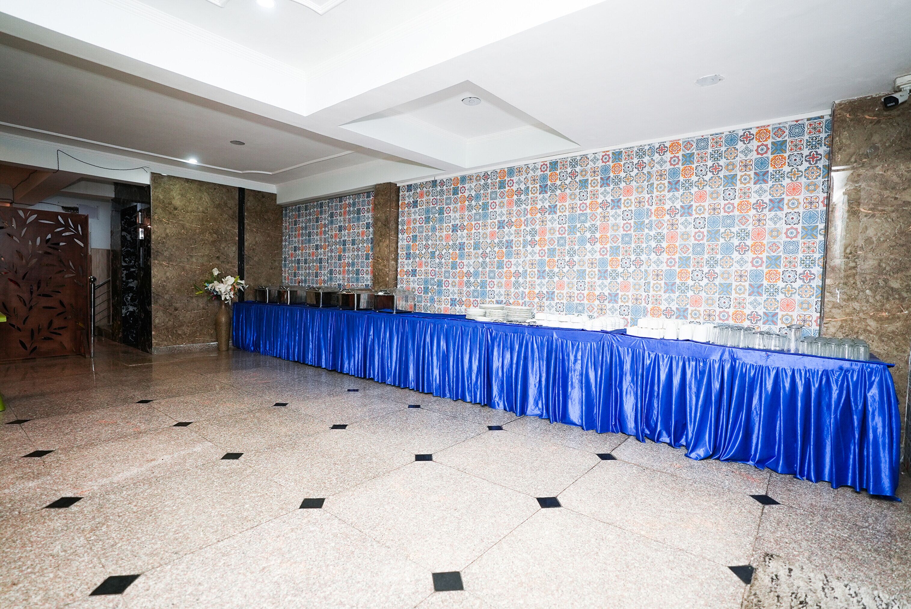 A spacious hall with a long blue table, patterned wall tiles, and a tiled floor.
