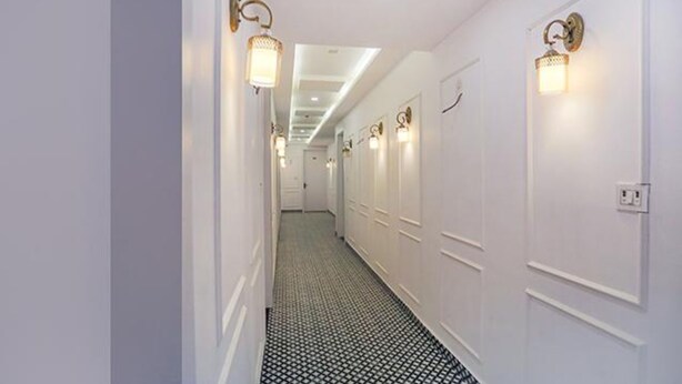 Un couloir aux murs blancs, au sol carrelé avec un motif noir et blanc, et doté de luminaires fixés au mur.