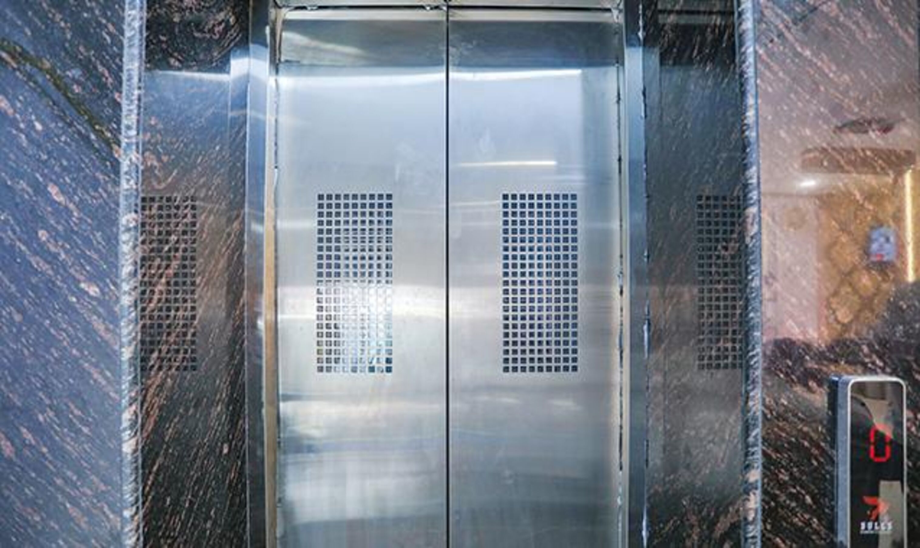 An elevator with metallic doors and ventilation grilles.