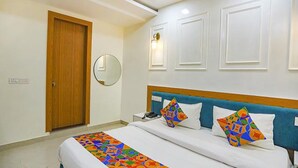 Une chambre d’hôtel avec un lit, une porte en bois, une lampe fixée au mur et un miroir.