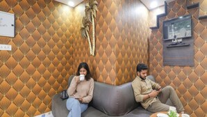 A room with a patterned wall, a sofa, a small table with a plant, and a television mounted on the wall. - FabHotel A One Inn (Lucknow)