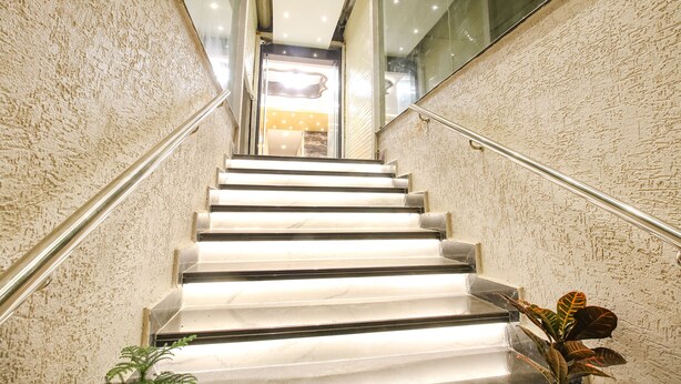 Un escalier avec un mur à texture et une main courante, menant à un espace bien éclairé avec une porte.