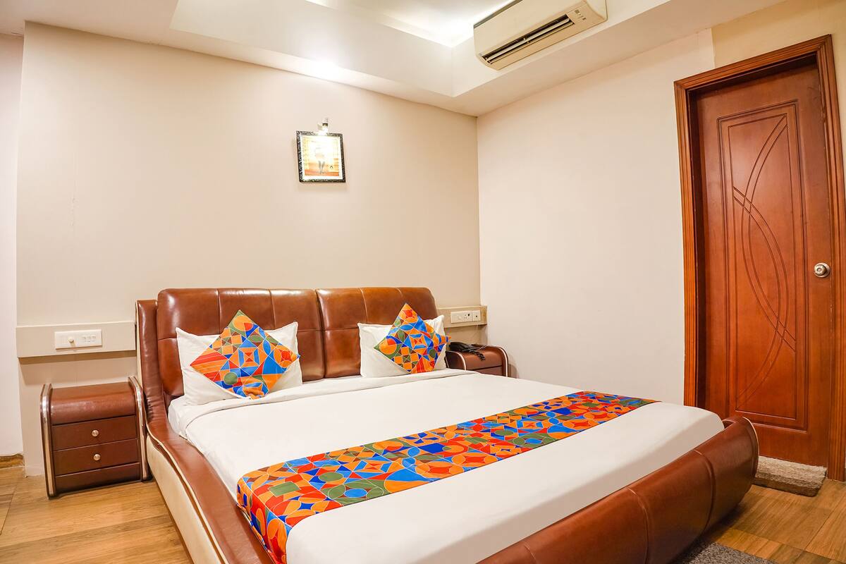 A hotel room with a large bed, a nightstand, a wooden door, and a wall-mounted air conditioner.