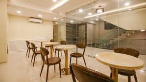 Un espace repas avec des tables et des chaises rondes, un escalier et une cloison en verre.