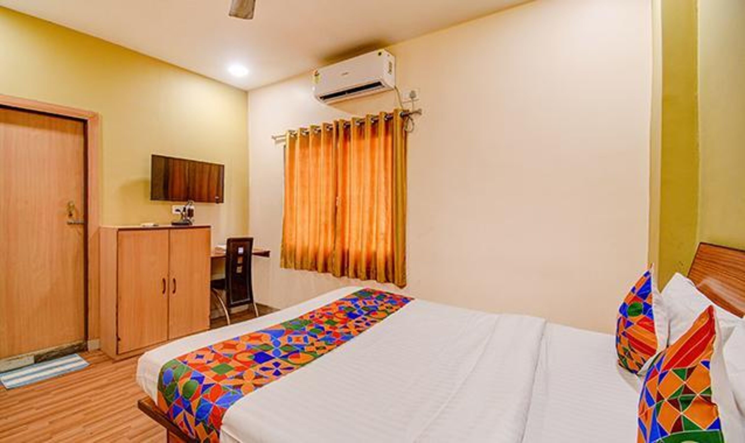 A hotel room with a bed, a desk, a wardrobe, and an air conditioning unit.