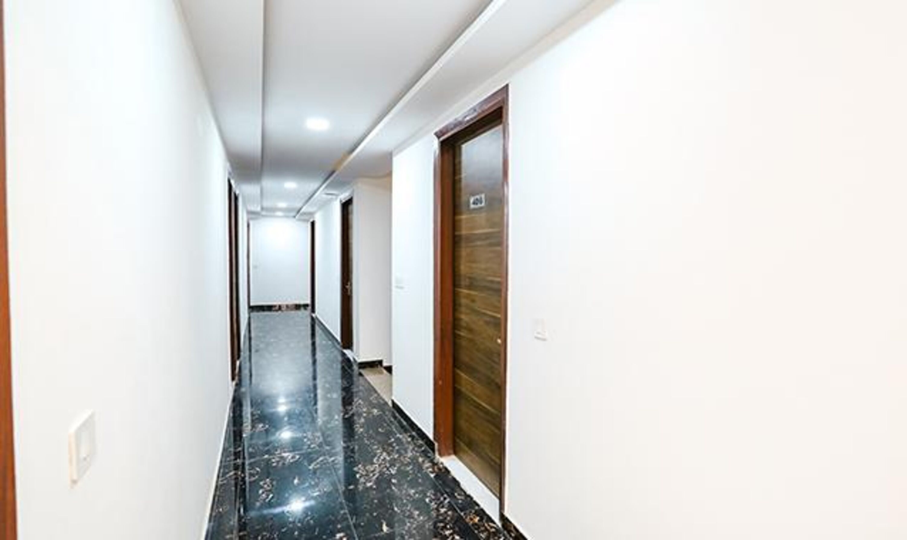 A long, narrow hallway with a marble floor, white walls, and a wooden door at the end.