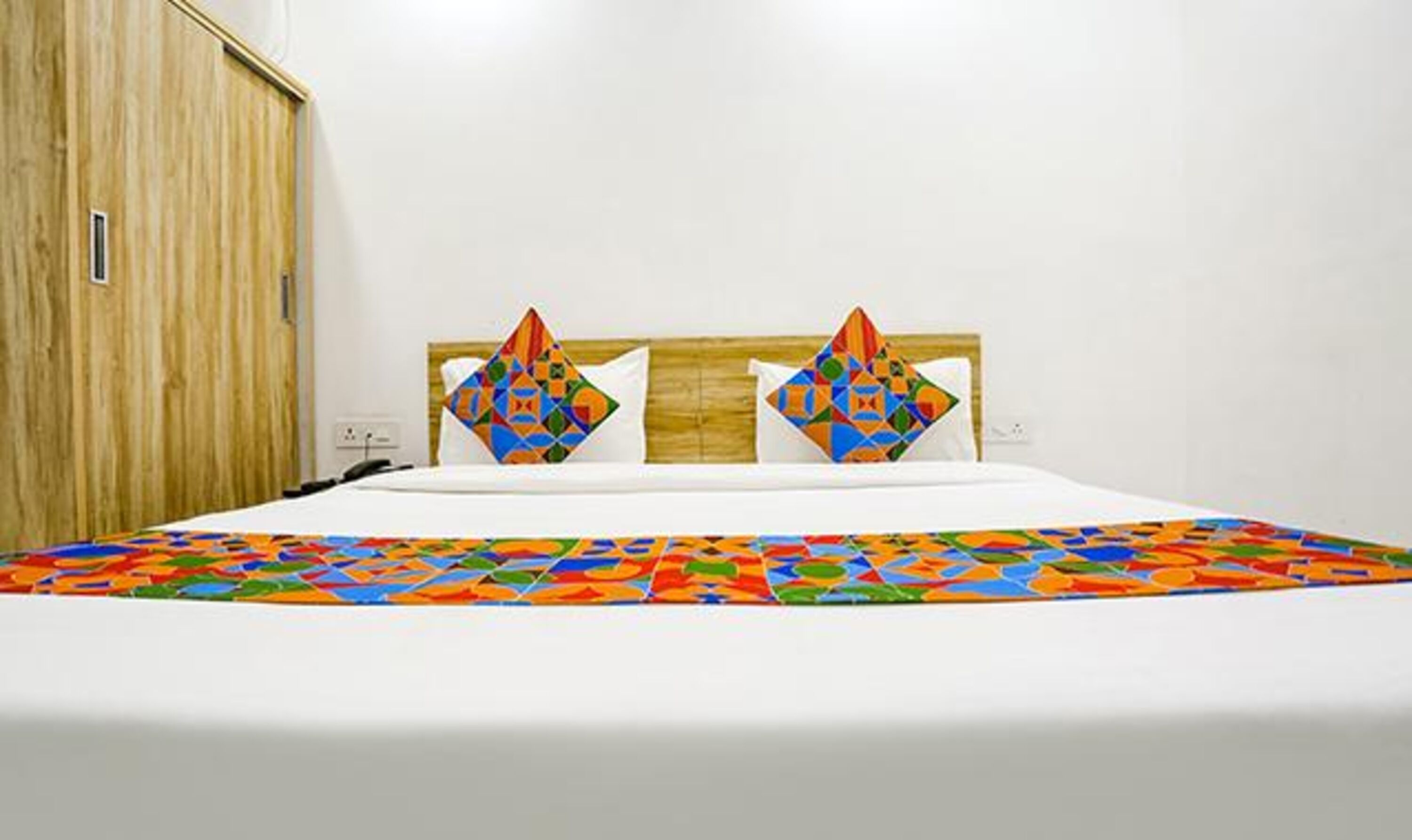 Una cama con un edredón colorido, un cabecero de madera y una pared blanca.