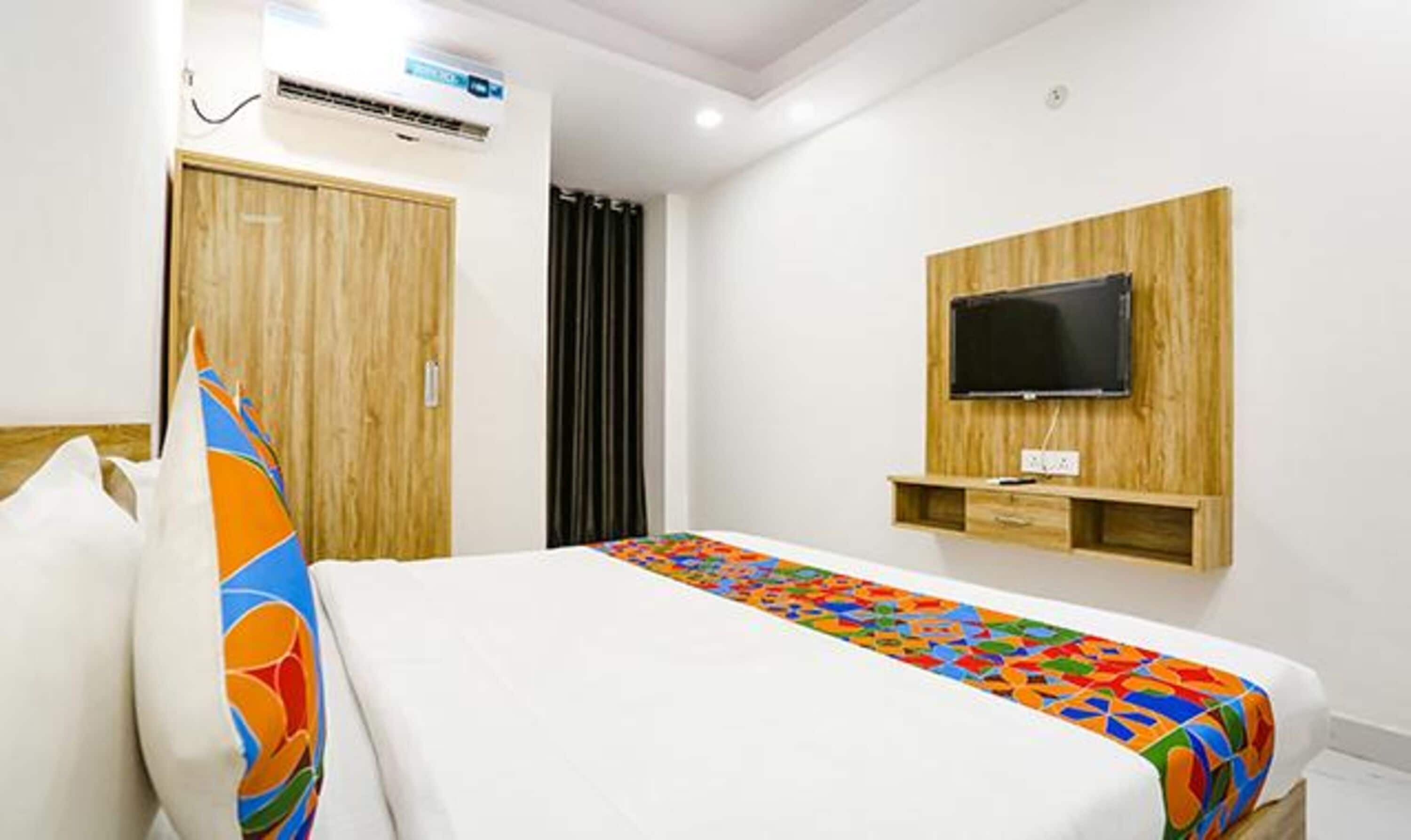 A hotel room with a bed, a TV mounted on the wall, and a wooden wardrobe.