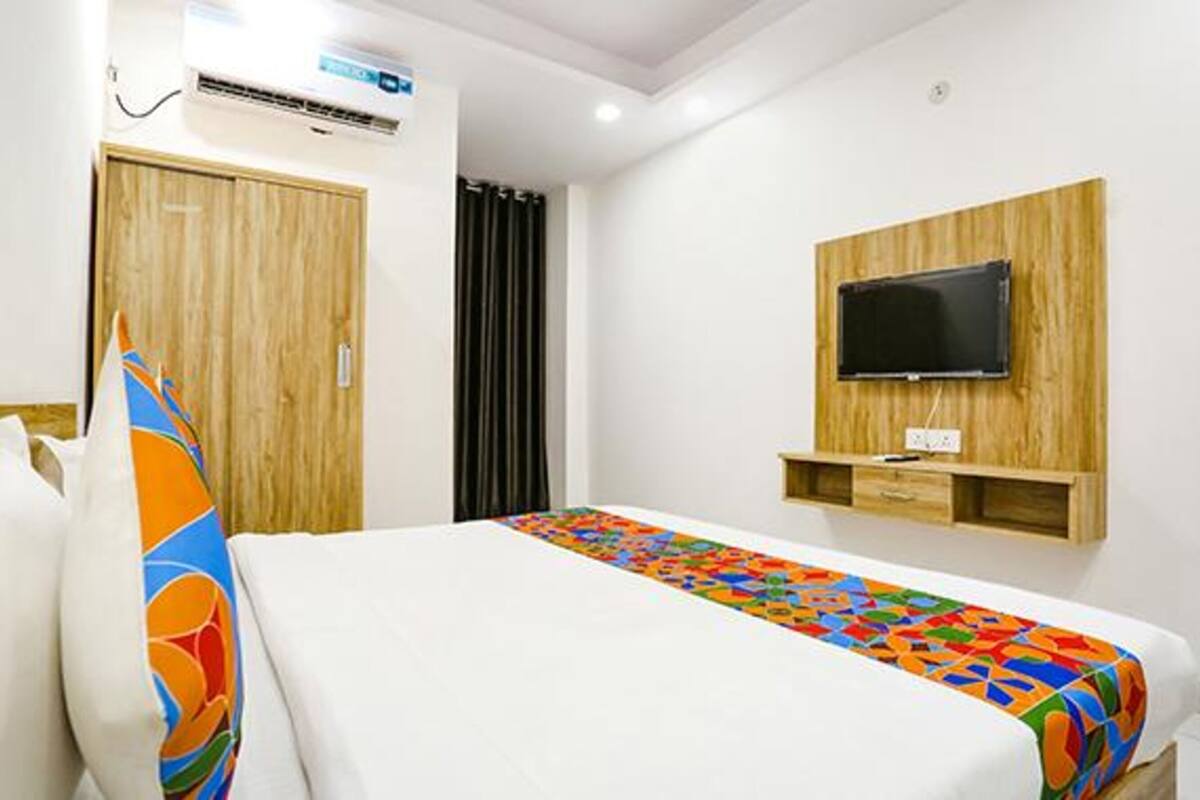 A hotel room with a bed, a TV mounted on the wall, and a wooden wardrobe.