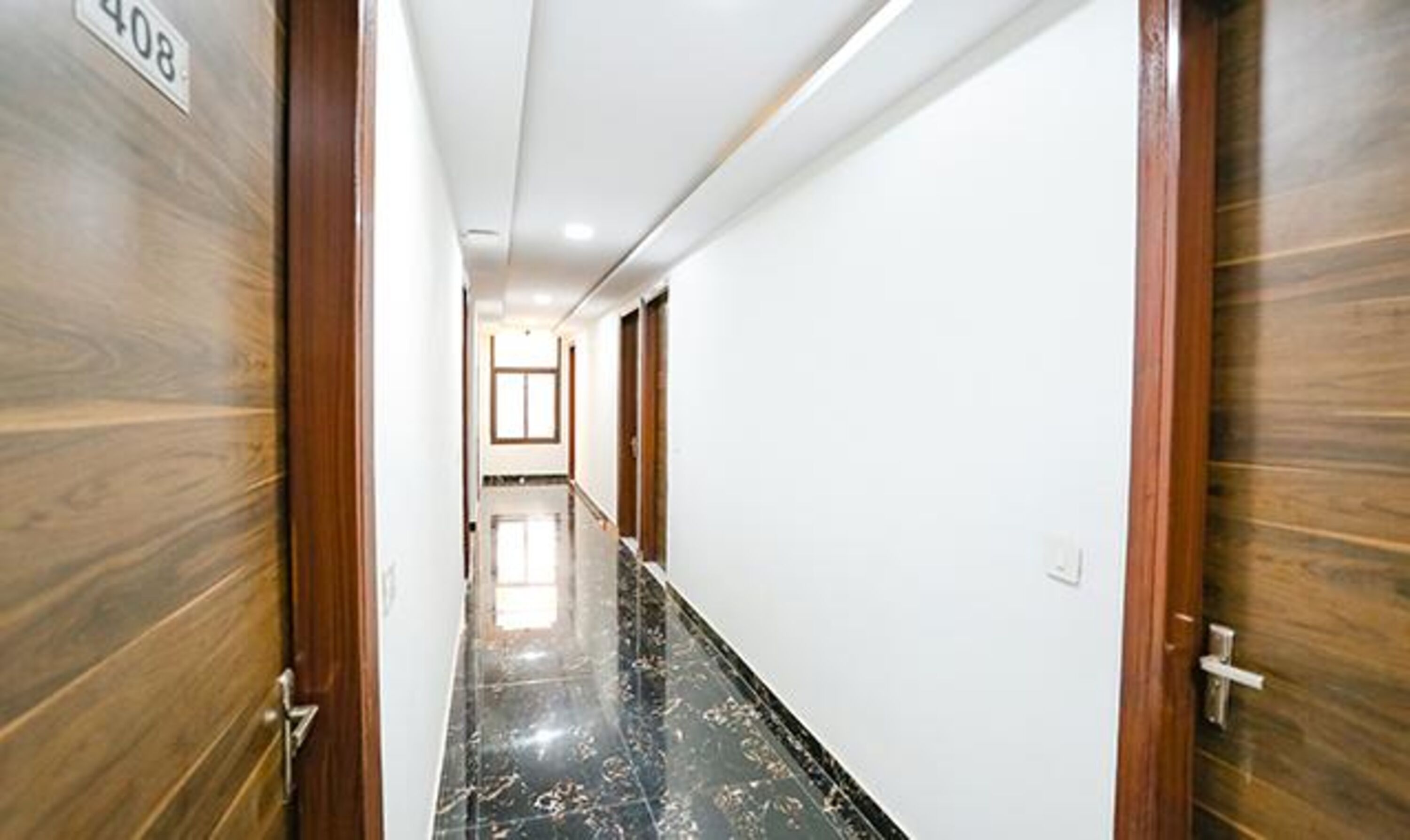 A hallway with wooden doors, white walls, and a shiny black floor.