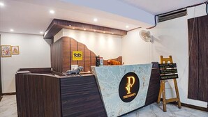 A reception desk with a marble top, a wooden panel design, and a logo for 'The Pannies'. There is a fan to the right and a small dog on the desk. - Fabhotel The Pannis (Bhopal)