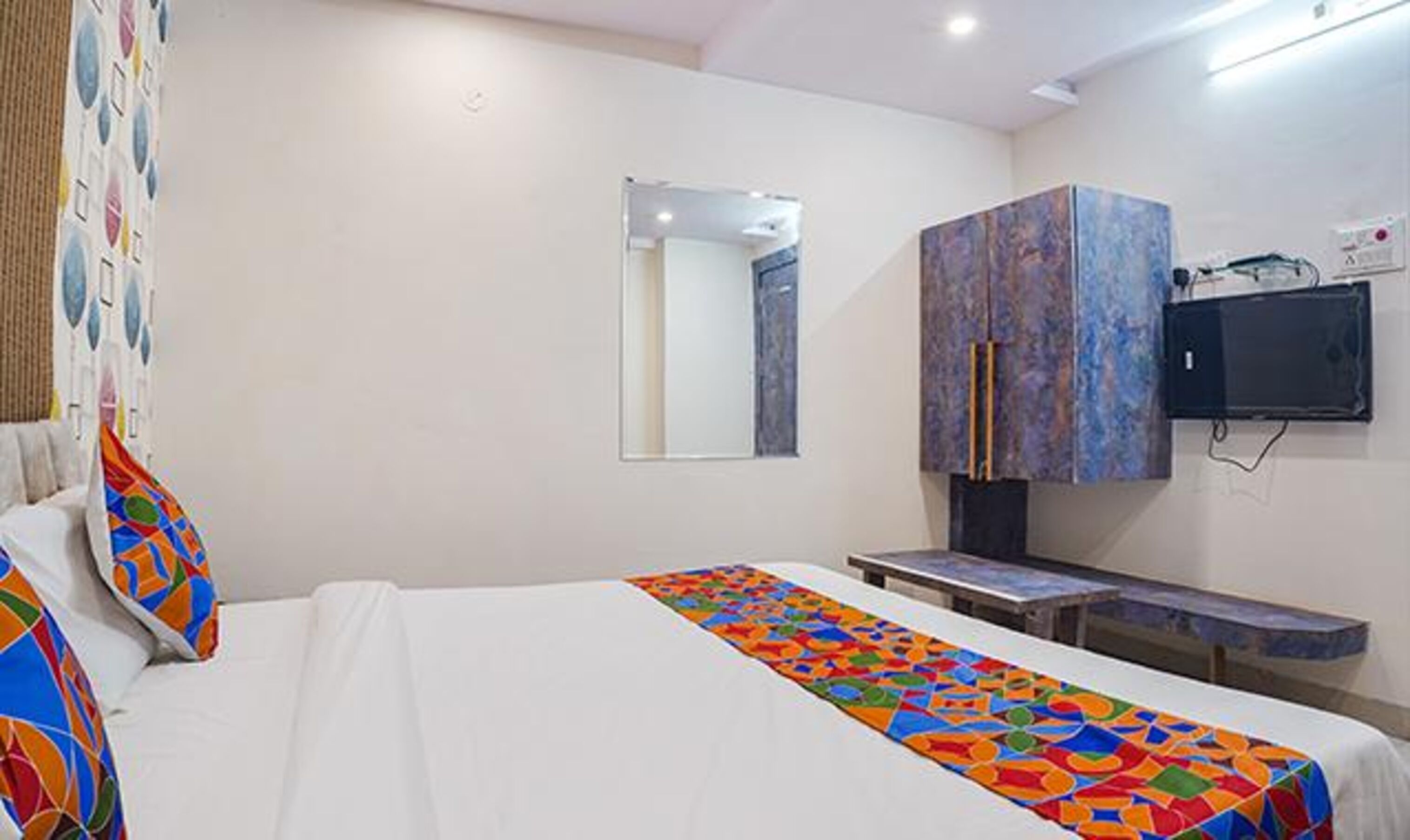 Una habitación de hotel con cama, televisión en la pared y un espejo.
