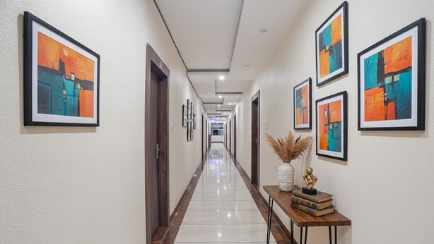 A hallway with framed abstract art on the walls, a polished floor, and a wooden bench with books and a vase. - Fabhotel The Pannis (Bhopal)