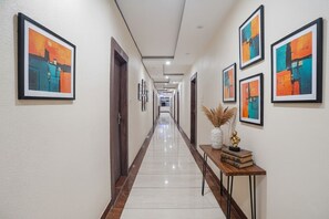 A hallway with framed abstract art on the walls, a polished floor, and a wooden bench with books and a vase. - Fabhotel The Pannis (Bhopal)