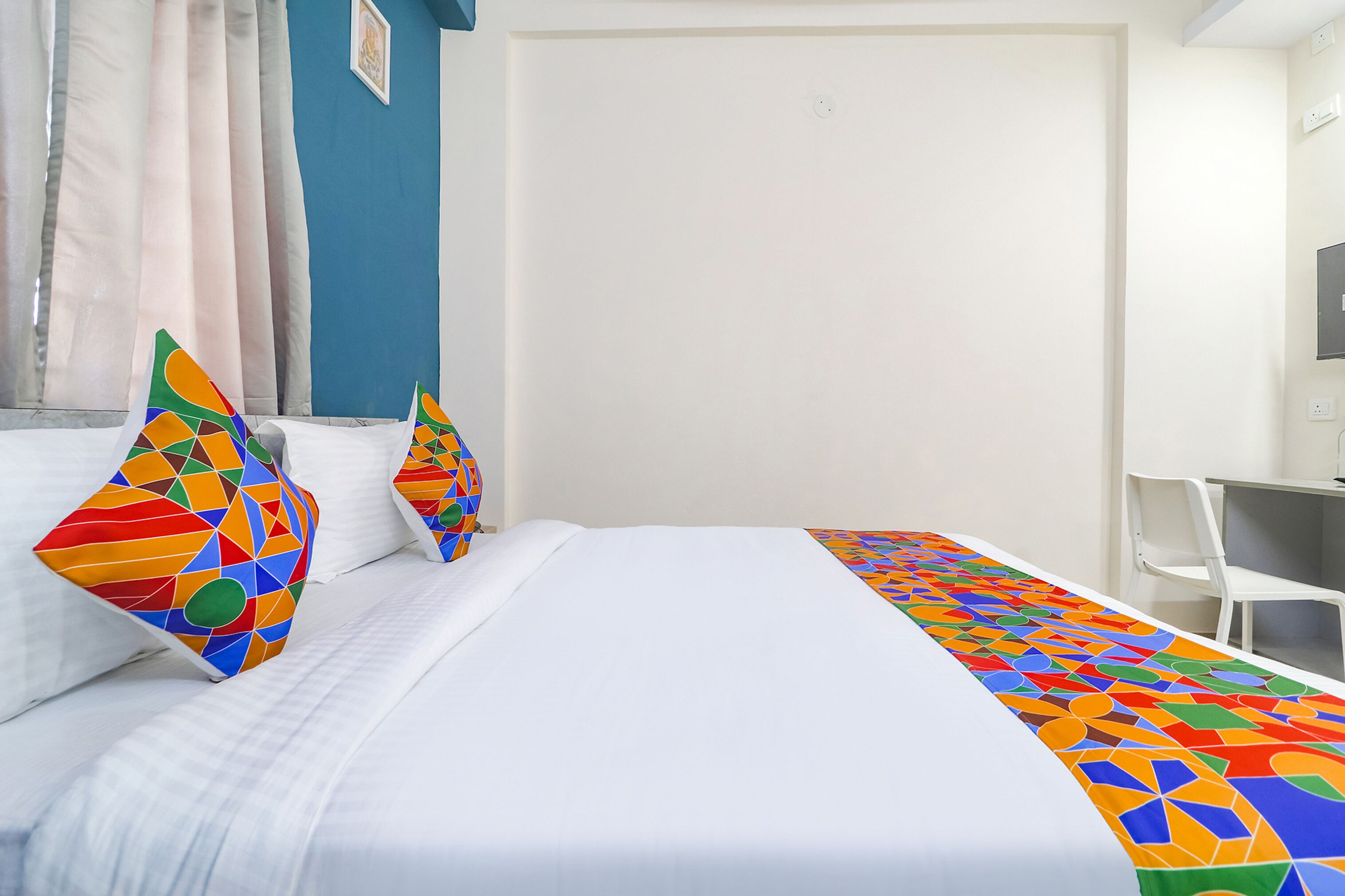 Una habitación de hotel con una cama bien hecha, un escritorio con silla y un amplio ventanal con cortinas.