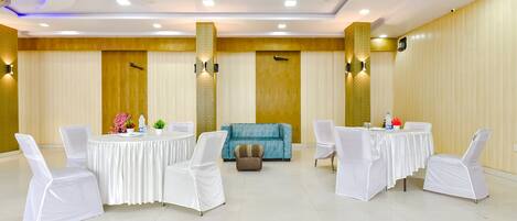 A conference room with white chairs, a round table, a sofa, and ceiling fans.