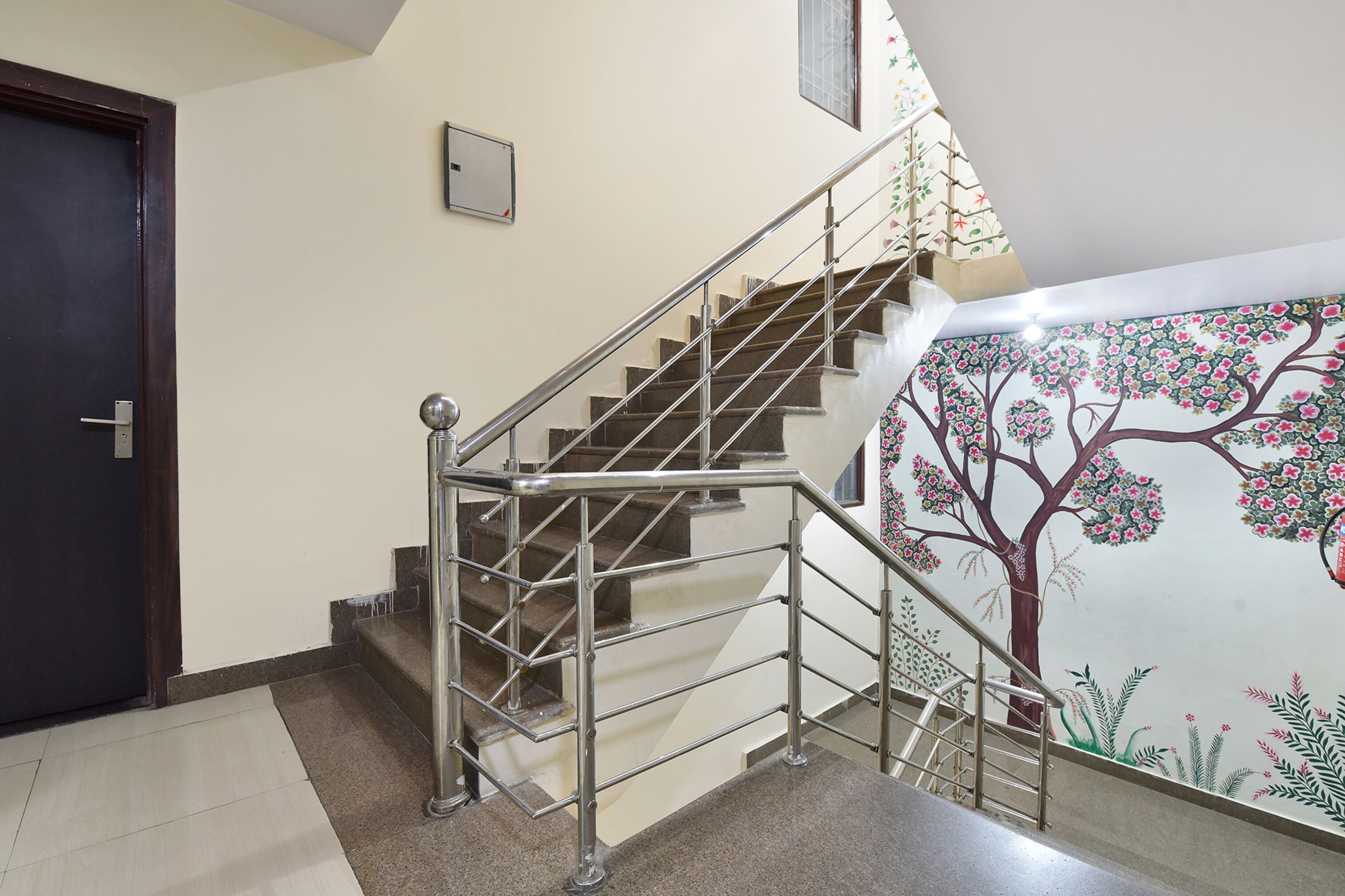 Una escalera con barandillas de metal, una puerta y una pared con un mural de un árbol.