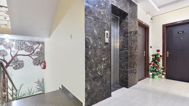 Vestíbulo de hotel con un ascensor de mármol, una escalera y un mural en la pared.