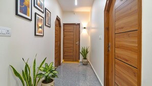 A hallway with wooden doors, framed artwork on the walls, and potted plants. - FabHotel SR Hitech City (Hyderabad)