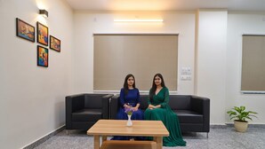 Two women seated on a black sofa in a room with a marble floor, a wooden table, and a potted plant. - FabHotel SR Hitech City (Hyderabad)