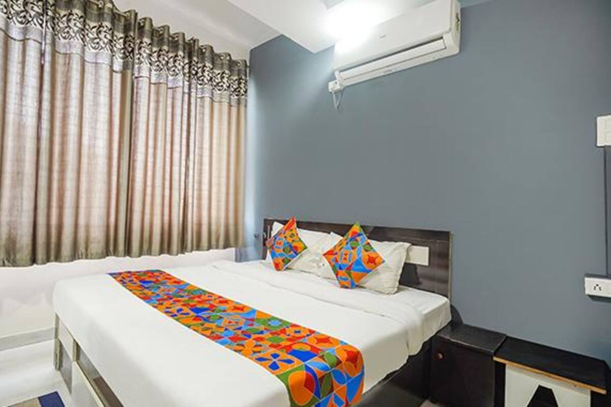 A hotel room with a large bed, a nightstand, a wall-mounted air conditioner, and a window with curtains.