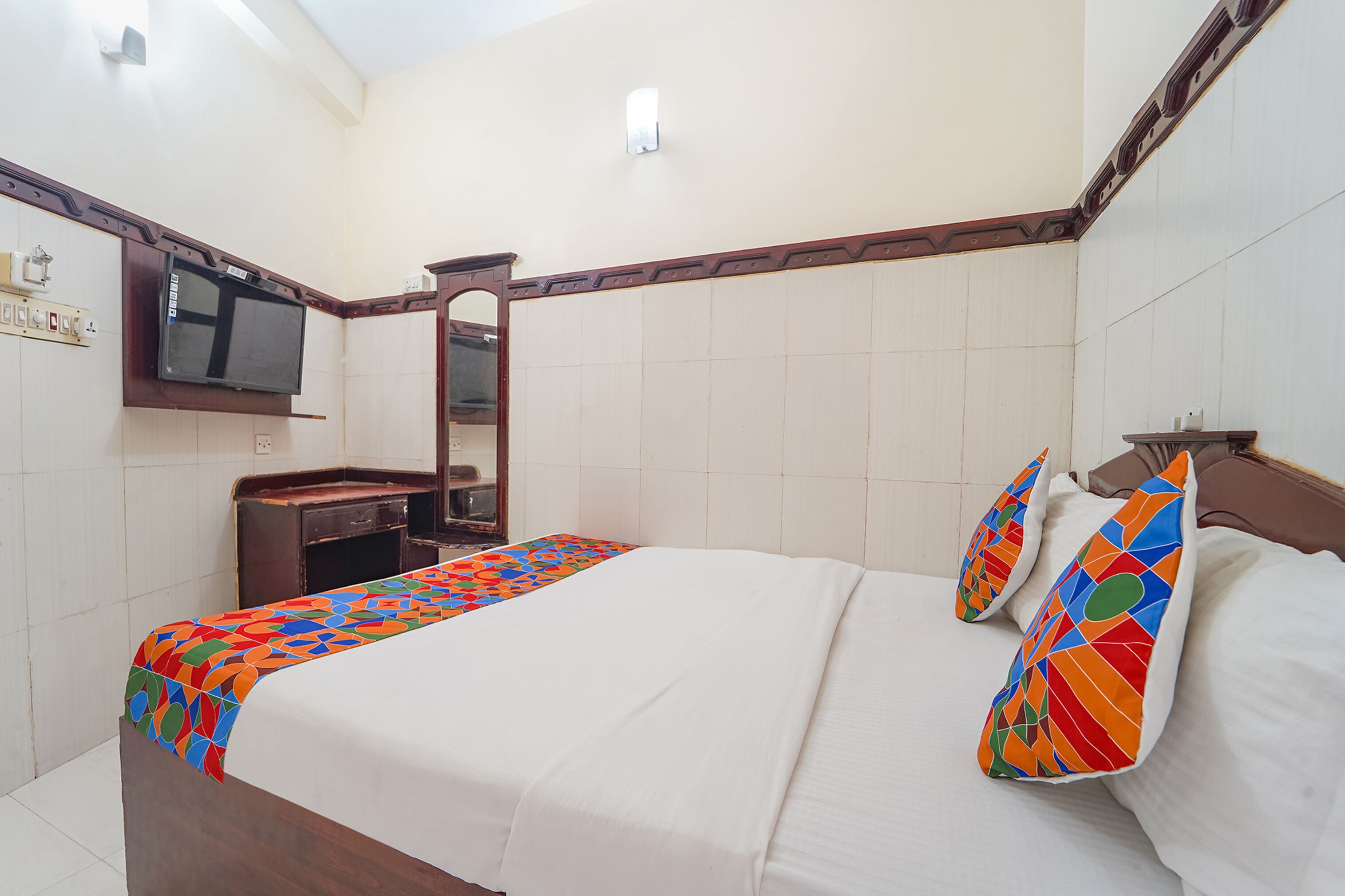 Una habitación de hotel con una cama, un televisor montado en la pared, un tocador y un espejo.