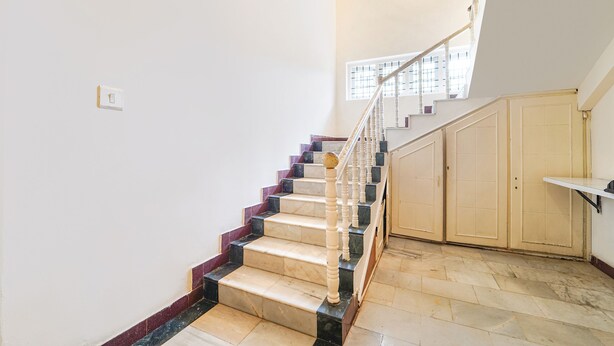 Una escalera con escalones de mármol y balaustres de madera, que conduce a un rellano con una ventana y una puerta.