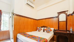 Habitación de hotel con cabecera de madera, cama con ropa de cama colorida, mesita de noche con una botella y un espejo.