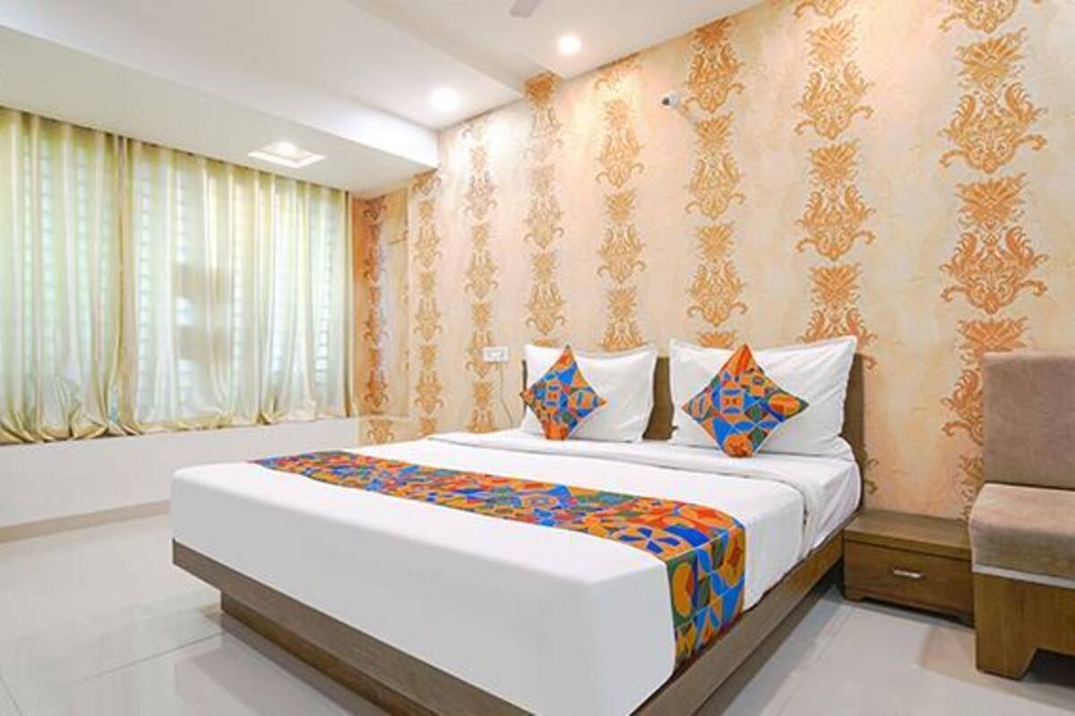 A hotel room with a large bed, a nightstand, a chair, and a window with curtains.