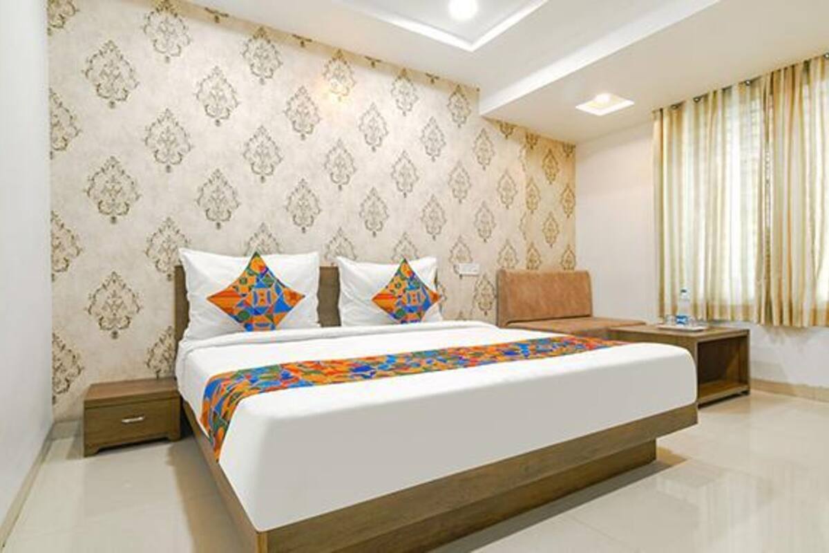 A modern hotel room with a large bed, patterned wallpaper, a nightstand, and a window with curtains.