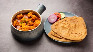 A bowl of orange curry with vegetables and a plate of flatbreads on a gray surface. - Fabhotel Shravan (Nagpur)