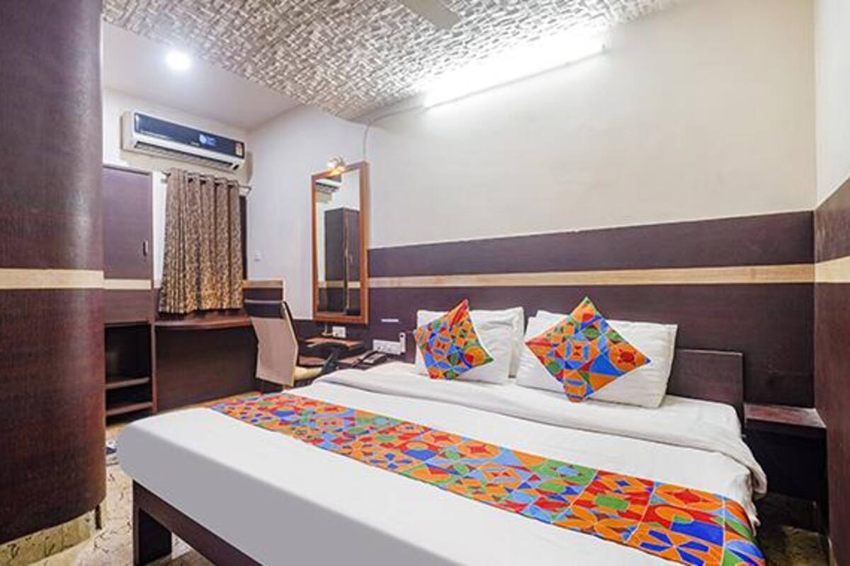 A hotel room with a bed, a desk, an air conditioning unit, and a mirror.