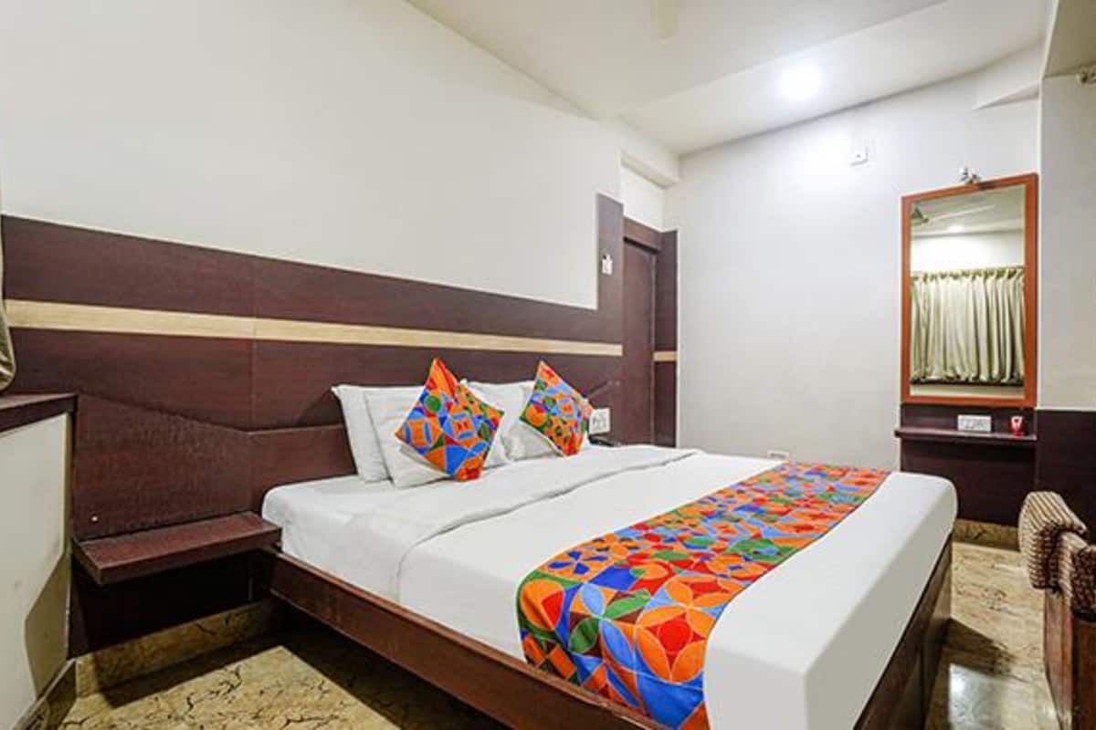 A hotel room with a bed, a nightstand, a mirror, and a window with curtains.