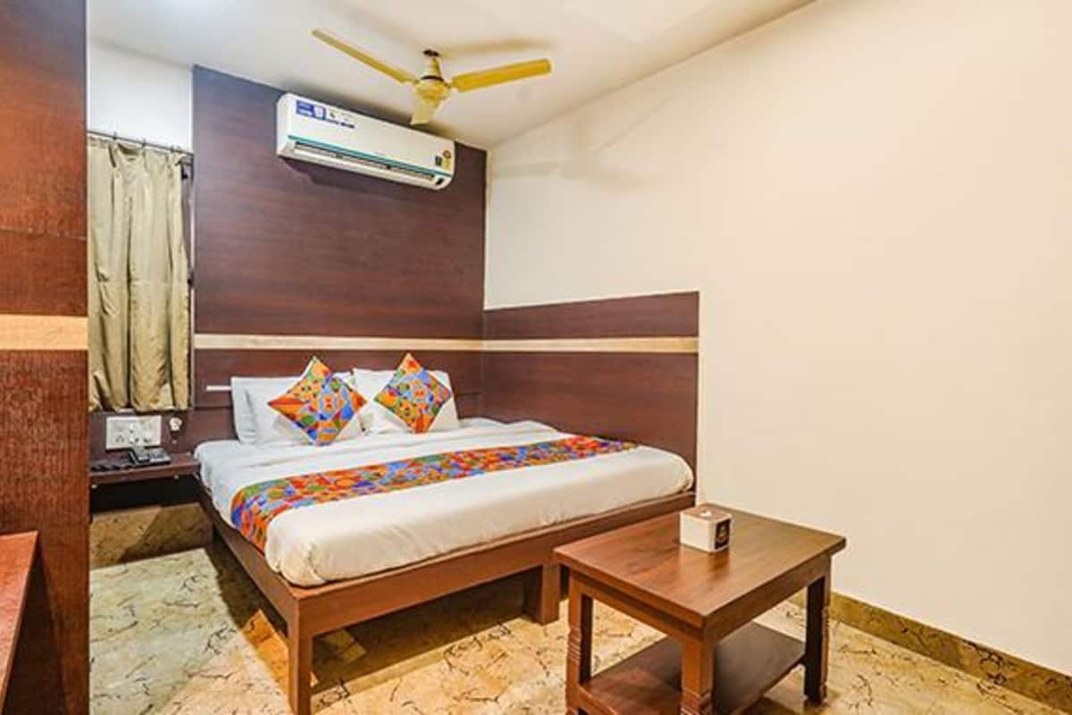 A hotel room with a wooden bed, a ceiling fan, an air conditioning unit, a bedside table, and a nightstand.
